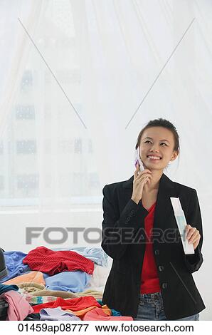 Young woman packing clothes while on the phone View Large Photo Image Stock Photo - Young woman packing clothes while on the phone. Fotosearch