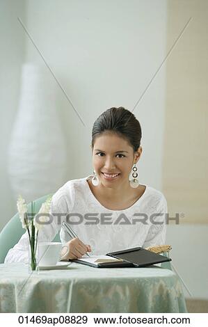 Stock Photo - Young woman sitting in restaurant, signing bill. Fotosearch