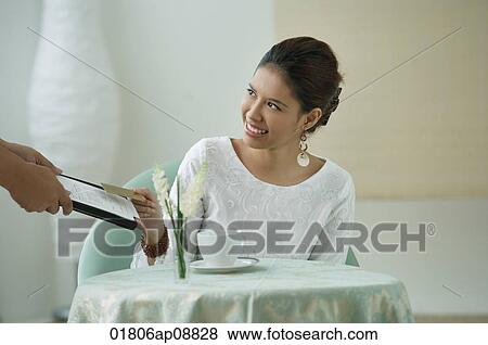 Young woman sitting in restaurant, being handed a menu View Large Photo Image Stock Photo - Young woman sitting in restaurant, being handed a menu. Fotosearch