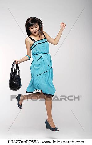 Young woman wearing blue dress, holding purse and jumping View Large Photo Image Stock Image - Young woman wearing blue dress, holding purse and jumping. Fotosearch