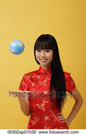 Stock Image - Young woman wearing red cheongsam and throwing globe in the air. Fotosearch