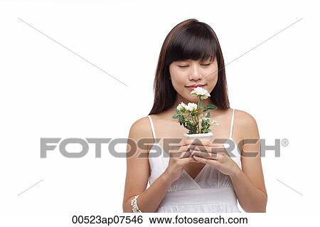 Young woman wearing white dress, holding small plant and smelling flower View Large Photo Image Stock Photograph - Young woman wearing white dress, holding small plant and smelling flower. Fotosearch