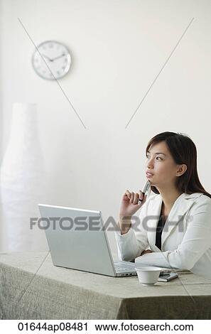 Stock Image - Young woman with laptop gazing into distance. Fotosearch