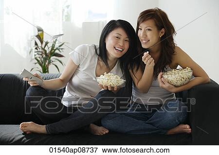 Young women enjoying popcorn on couch View Large Photo Image Stock Photo - Young women enjoying popcorn on couch. Fotosearch