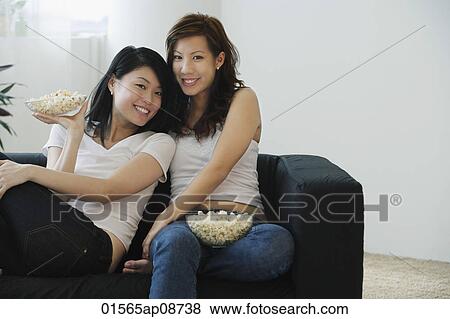 Young women enjoying popcorn on couch View Large Photo Image Stock Photo - Young women enjoying popcorn on couch. Fotosearch