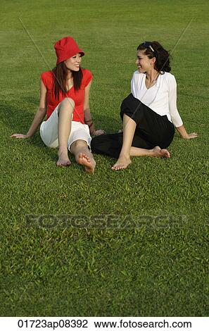 Stock Image - Young women in park, looking at each other. Fotosearch