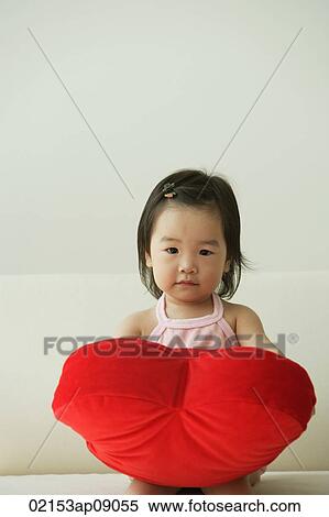 Stock Photography - Baby girl with heart-shaped cushion. Fotosearch