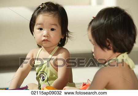 Baby girls sitting and one looking at camera View Large Photo Image Stock Image - Baby girls sitting and one looking at camera. Fotosearch