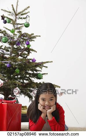 Girl elbow on ground with Christmas present and Christmas tree at the background View Large Photo Image Stock Photograph - Girl elbow on ground with Christmas present and Christmas tree at the background. Fotosearch