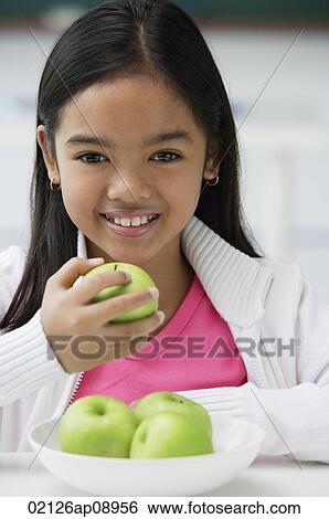 Stock Photograph - Girl holding green apple in one hand smiling at camera. Fotosearch