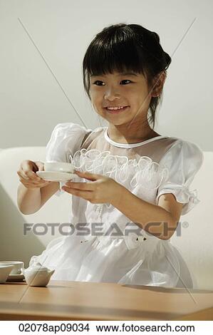 Picture - Girl in white dress playing with tea cups. Fotosearch