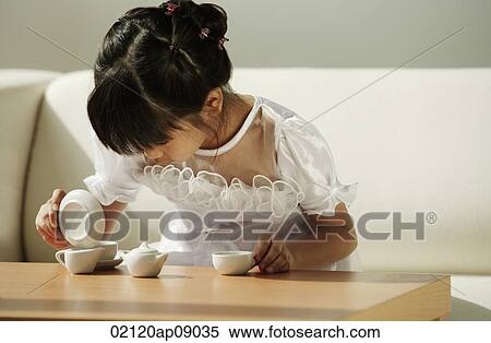 Stock Photography - Girl in white dress playing with tea cups. Fotosearch