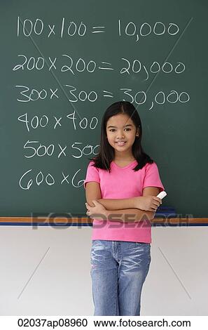 Stock Image - Girl with chalk on hand standing in front of blackboard. Fotosearch