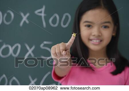 Stock Image - Girl with star on finger standing in front of blackboard. Fotosearch
