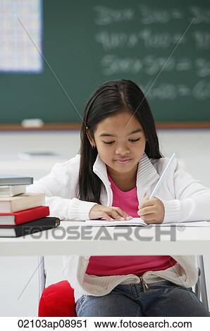 Stock Image - Girl writing and sitting at school desk. Fotosearch