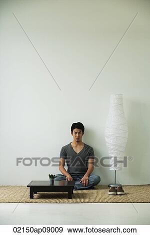 Serious young man sitting on floor, looking at camera View Large Photo Image Stock Photo - Serious young man sitting on floor, looking at camera. Fotosearch