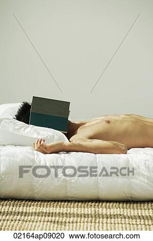Young man lying in bed, face covered by a book View Large Photo Image Stock Image - Young man lying in bed, face covered by a book. Fotosearch