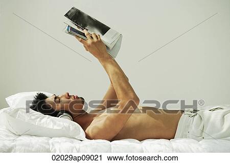 Young man lying in bed, reading and listening to music View Large Photo Image Stock Image - Young man lying in bed, reading and listening to music. Fotosearch