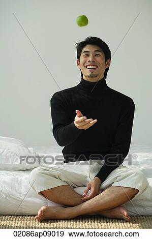 Young man sitting on bed, throwing apple in the air View Large Photo Image Stock Photo - Young man sitting on bed, throwing apple in the air. Fotosearch