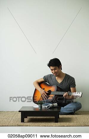 Young man sitting on floor and playing guitar View Large Photo Image Stock Image - Young man sitting on floor and playing guitar. Fotosearch