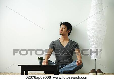 Young man sitting on floor looking up View Large Photo Image Stock Photograph - Young man sitting on floor looking up. Fotosearch