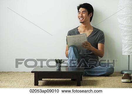 Stock Image - Young man sitting on floor while writing. Fotosearch