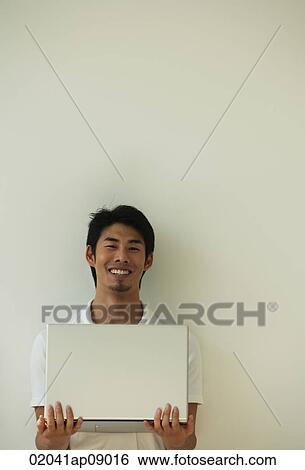 Stock Photograph - Young man with laptop on hands smiling at camera. Fotosearch