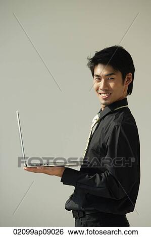 Young man with laptop on one hand smiling at camera View Large Photo Image Stock Photograph - Young man with laptop on one hand smiling at camera. Fotosearch