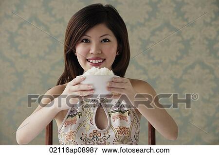 Stock Photo - Young woman raising bowl of rice smiling at camera. Fotosearch