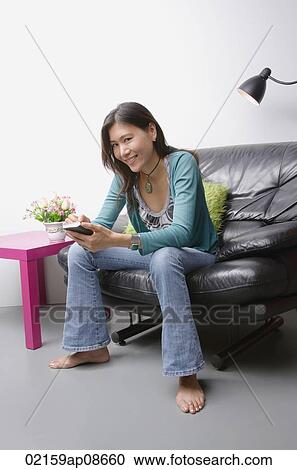 Stock Image - Young woman sitting on couch using organizer. Fotosearch