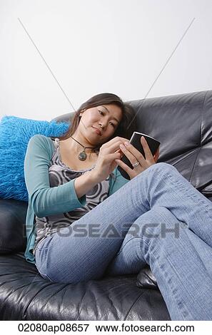 Young woman sitting on couch using organizer View Large Photo Image Stock Photo - Young woman sitting on couch using organizer. Fotosearch