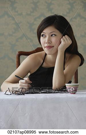 Stock Photography - Young woman with journal staring thoughtfully into distance. Fotosearch