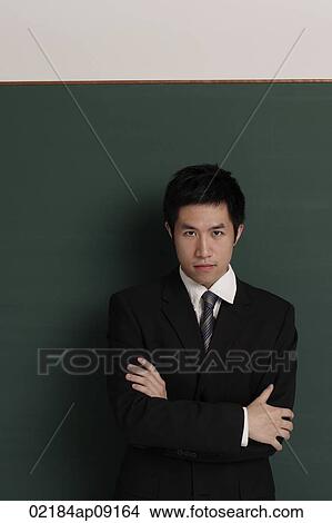 Picture - Businessman standing against black wall with arms crossed. Fotosearch