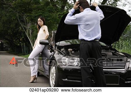 Man looking under car hood of broken down car, woman waiting View Large Photo Image Stock Image - Man looking under car hood of broken down car, woman waiting. Fotosearch