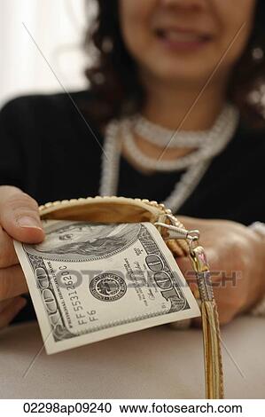 Stock Image - woman removing $100 dollar bill from her purse. Fotosearch