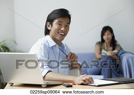 Young couple at home; man at desk, woman with book on couch View Large Photo Image Picture - Young couple at home; man at desk, woman with book on couch. Fotosearch