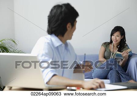Young couple at home; man at desk, woman reading View Large Photo Image Stock Image - Young couple at home; man at desk, woman reading. Fotosearch