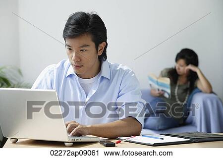 Young couple at home; man on computer, woman reading View Large Photo Image Stock Image - Young couple at home; man on computer, woman reading. Fotosearch