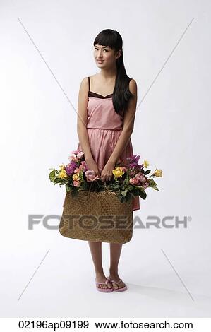 Stock Photo - Young woman holding straw bag full of flowers. Fotosearch