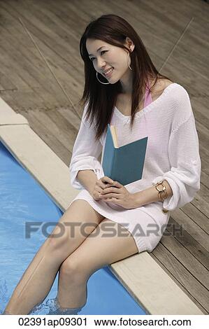 Stock Image - Young woman reading poolside. Fotosearch