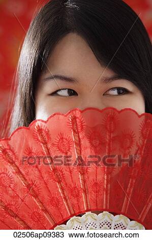 Stock Image - Chinese woman looking over hand-held fan. Fotosearch