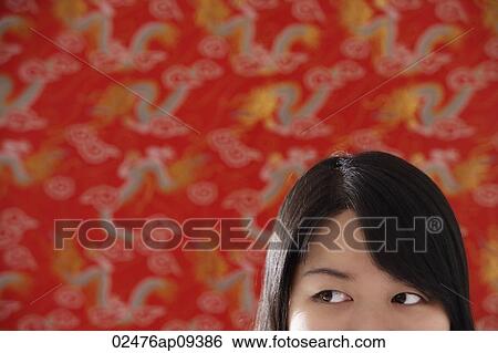 Stock Photograph - Cropped face of Chinese woman standing against Chinese silk background. Fotosearch