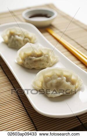 Stock Image - 3 steamed gyoza dumplings placed on white plate with sauce on the side. Fotosearch
