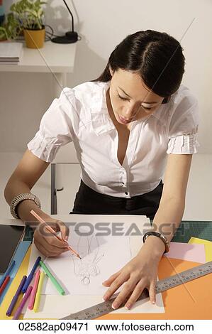 Stock Image - Chinese fashion designer sketching at work desk. Fotosearch