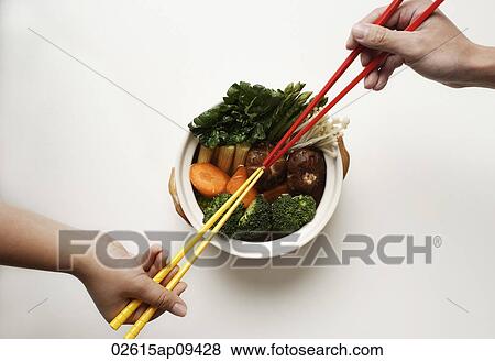 Stock Photo - hands holding chopsticks in clay pot of vegetables. Fotosearch