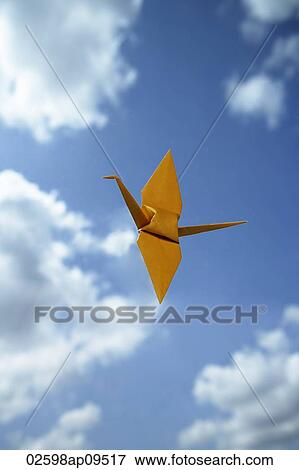 Stock Photo - single yellow paper crane against sky backdrop. Fotosearch