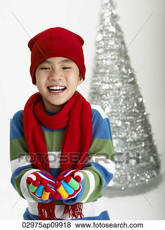 Stock Photo - boy dressed in winter clothes in front of christmas tree. Fotosearch
