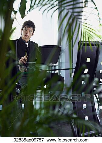 "businessman sitting at table, plants in foreground" View Large Photo Image Stock Photo - "businessman sitting at table, plants in foreground". Fotosearch