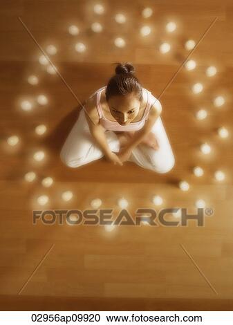 Stock Image - girl meditating surrounded by candles. Fotosearch