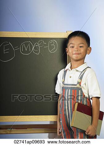 Stock Image - little boy in striped jumper standing before chalk board. Fotosearch